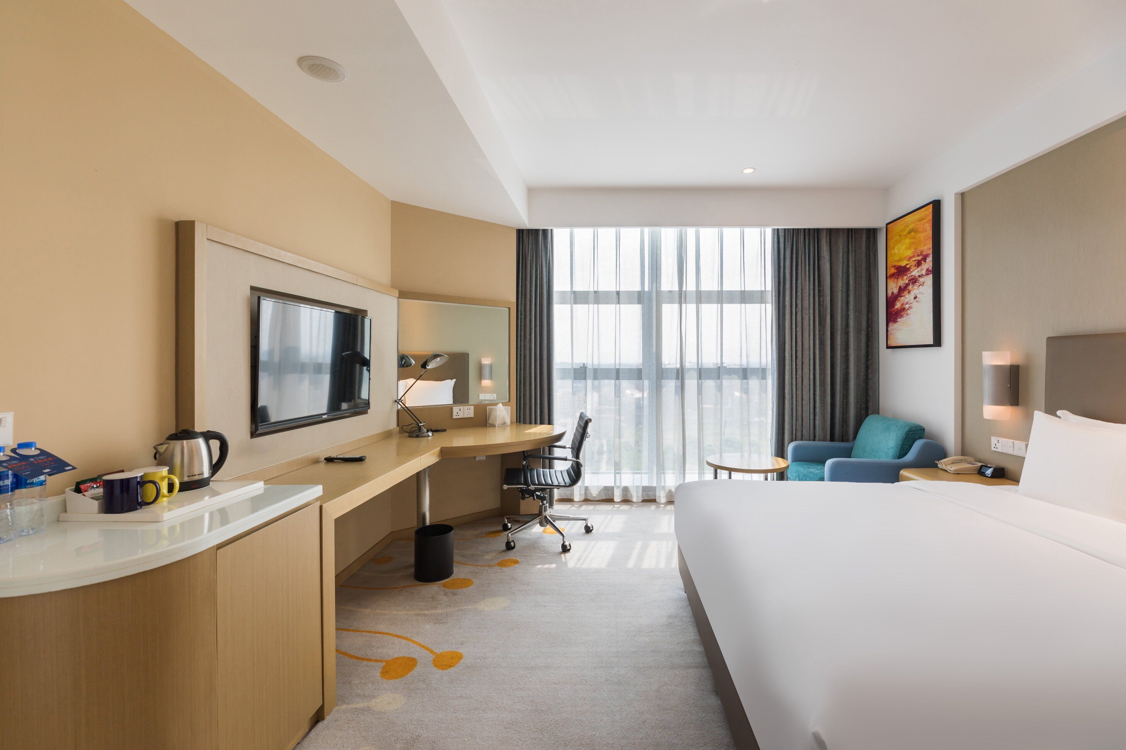 A hotel room with a bed, desk, chair, TV, and a large window.