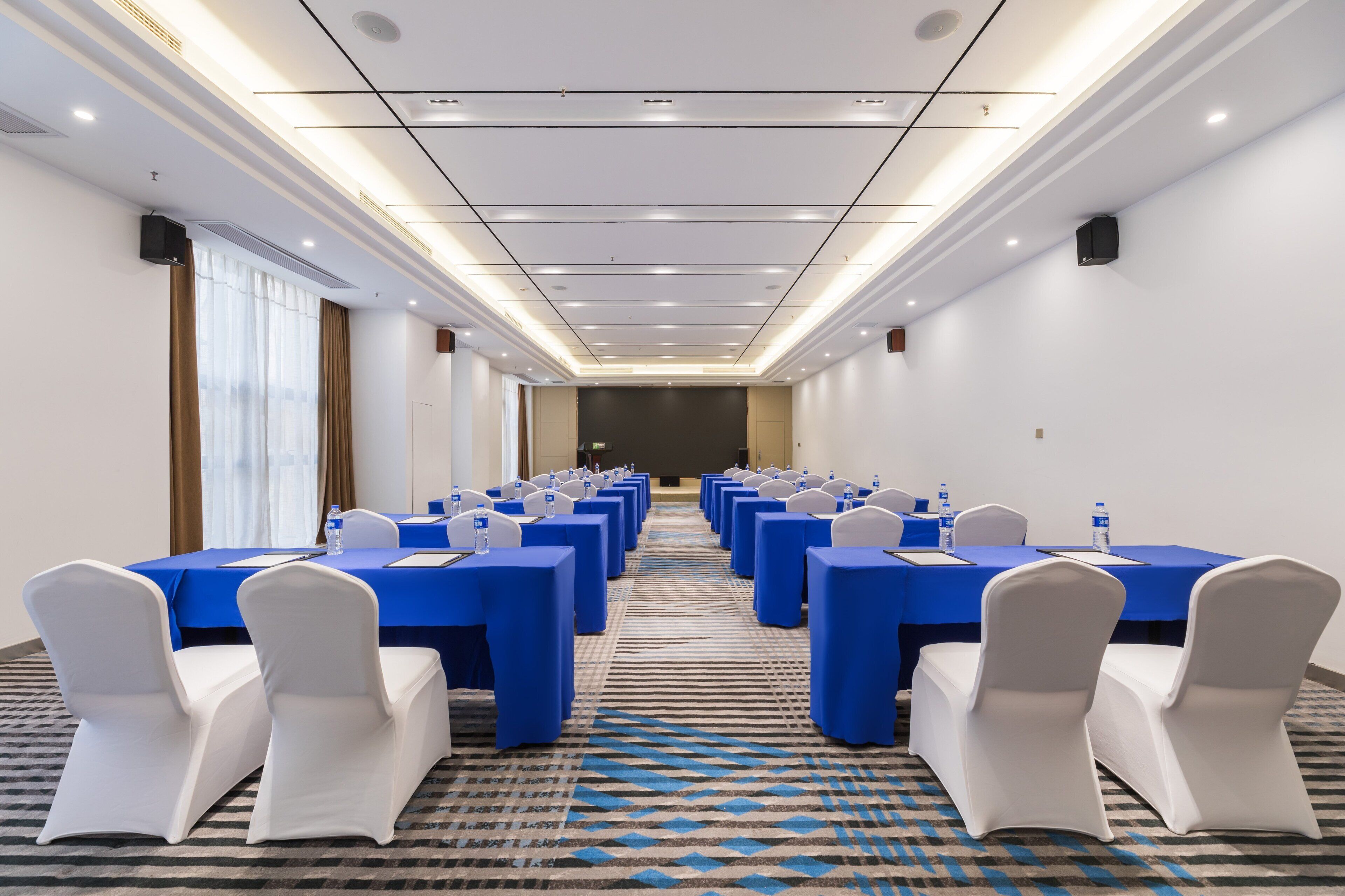 A conference room with rows of tables, chairs, and a carpeted floor.