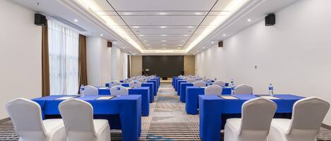 A conference room with rows of tables, chairs, and a carpeted floor.