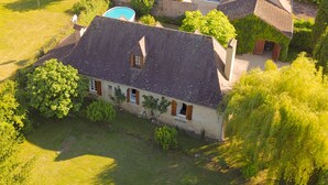 Vista aérea de una casa con techo inclinado, rodeada de vegetación exuberante y una piscina.