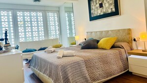 A modern bedroom with a large bed, a nightstand, a bedside lamp, and a window with a view.