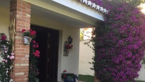 Een huis met een bakstenen gevel, een overdekte veranda en diverse potplanten en bloemen.