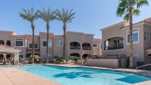Un área de piscina con una pileta azul cristalina, rodeada de edificios de varios pisos con balcones y palmeras.