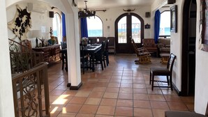 A spacious living area with a dining table, chairs, a sofa, and a view of the sea through large windows.