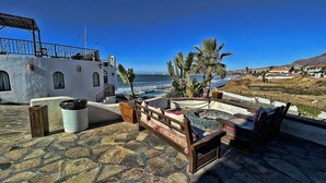 A terrace with a stone floor, a wooden bench, a small pool, and a view of the ocean.