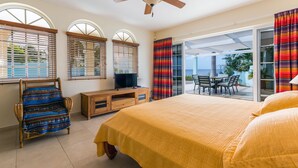 A bedroom with a bed, a TV, a wooden dresser, a chair, and a balcony with a table and chairs. - Tropical oceanfront villa, full AC, private pool, great diving and snorkeling (Kralendijk)