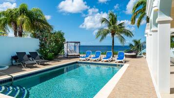 A pool area with lounge chairs and a view of the ocean.
