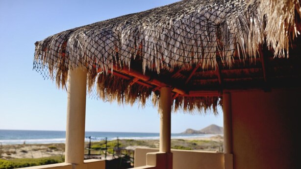 A thatched roof structure with a view of the beach and ocean.