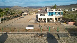 A beachside hotel with a pool area, a building with a blue and white facade, and a view of the beach and mountains in the background.
