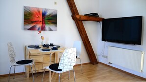 A room with a wooden dining table, two chairs, a television, and a radiator.