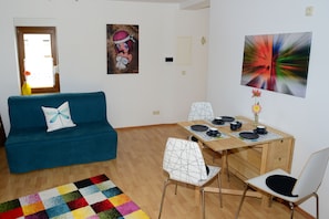 A living room with a blue sofa, a wooden dining table with chairs, and a colorful rug. - Apartment in Franconian Tuscany at the gates of the world cultural heritage (Memmelsdorf OT Laubend)