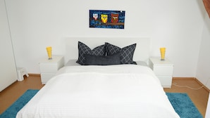 A bedroom with a bed, white nightstands, a night lamp, a painting, and a blue rug.