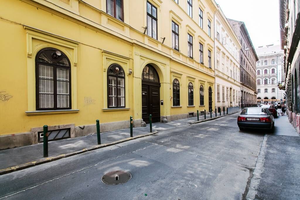 A narrow street with yellow buildings, a car parked on the side, and a pedestrian walkway.