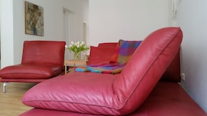 A red sofa and chair in a room with a small table and a vase of white flowers. - Spacious living on 54 sqm in the Palais am Schlossplatz - in the old town (Meersburg)