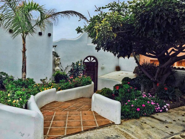 Un patio con piso de baldosas, una palmera y diversas plantas con flores.