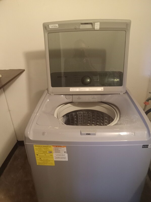Lavadora compacta gris con puerta frontal, panel de control y una etiqueta amarilla con texto.