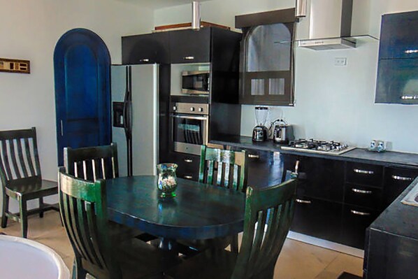 A modern kitchen with a dining table, chairs, a refrigerator, oven, and a stove.