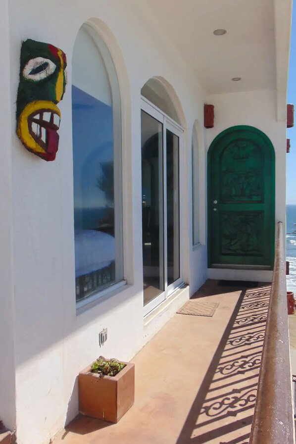 Un pasillo de hotel con una puerta verde, ventanas arqueadas y una barandilla de metal decorativa.