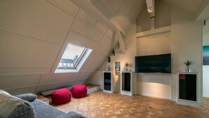A modern loft bedroom with a sloped ceiling, a skylight, a flat-screen TV, built-in shelving, and a wooden parquet floor. - THE ROOF Penthouse in the heart of Karlsruhe (Karlsruhe)