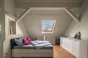 A bedroom with a sloped ceiling, a skylight, a bed with pillows, a dresser, and a mirror.