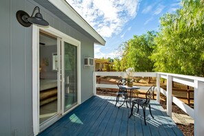 Une terrasse extérieure couverte, dotée d’une table et de chaises, d’une rambarde blanche et d’une porte-fenêtre coulissante donnant sur une pièce.