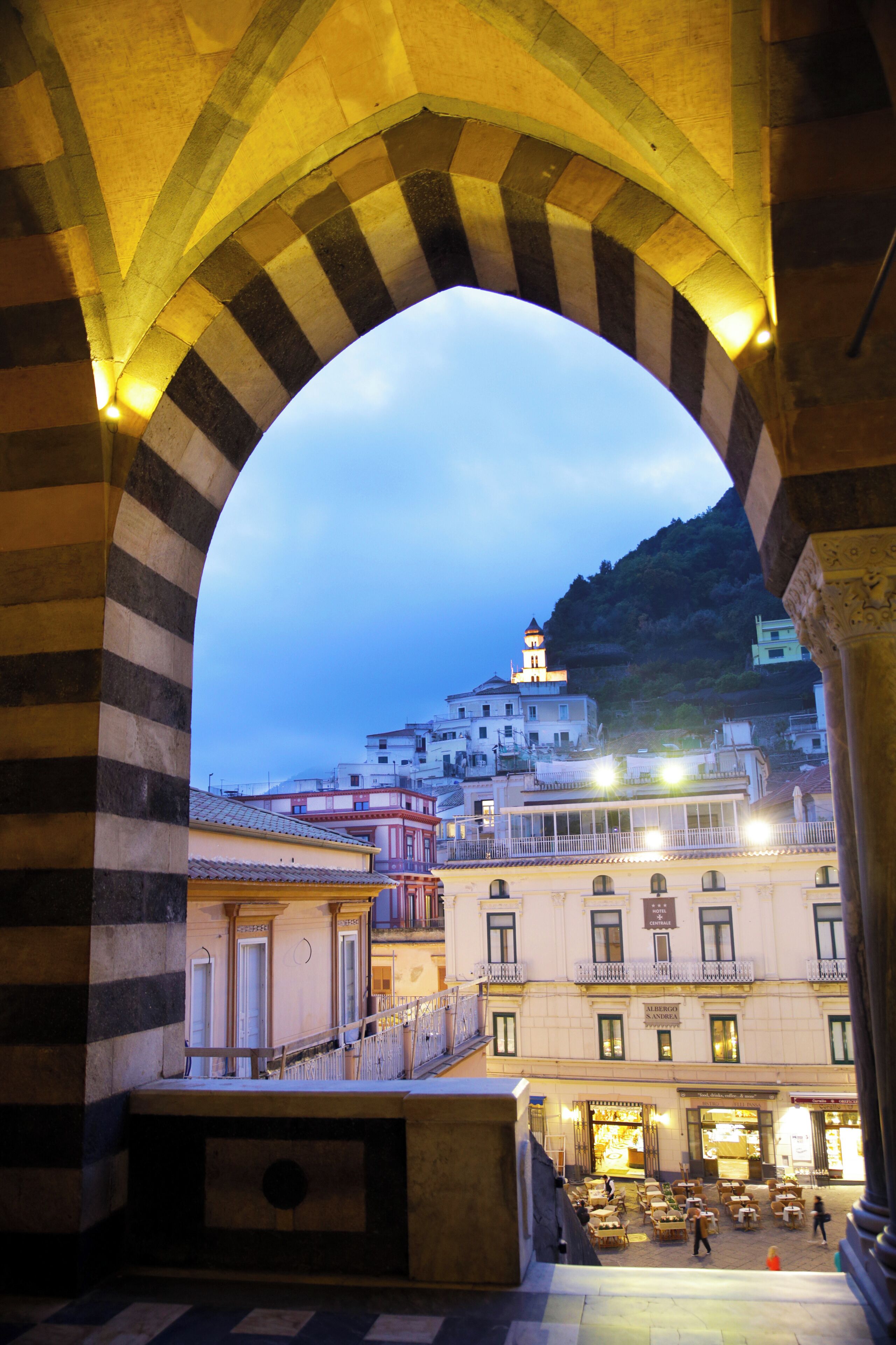 An arched architectural structure with a view of a town, including buildings and a hill in the background.
