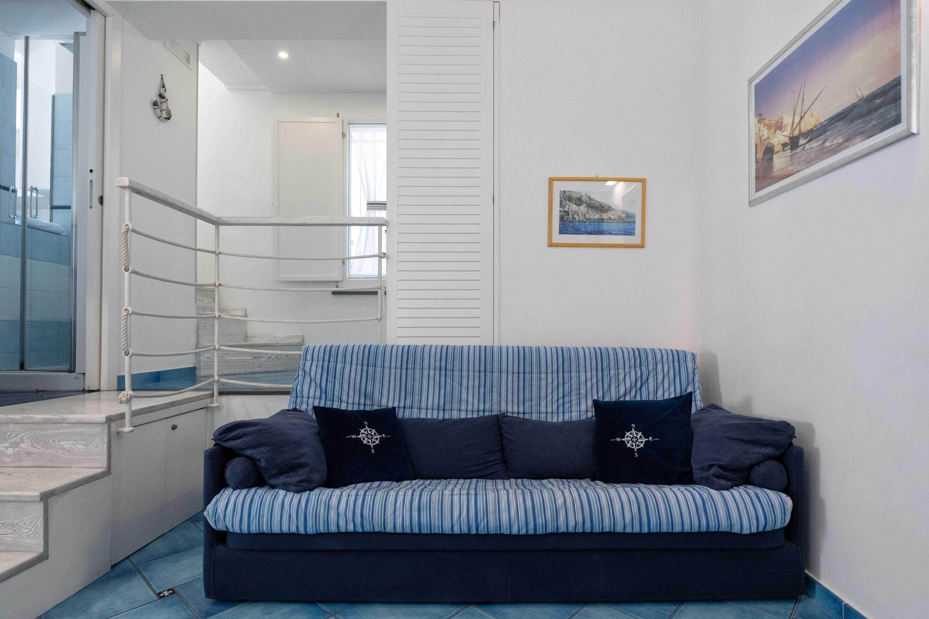 A room with a striped sofa, a staircase, a framed picture on the wall, and a door.