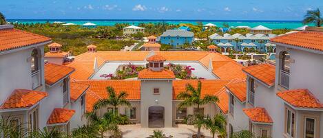 Un resort con varias edificaciones con tejados de tejas rojas y un patio central con palmeras.