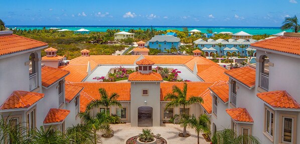 A resort with multiple buildings featuring red-tiled roofs and a central courtyard with palm trees.