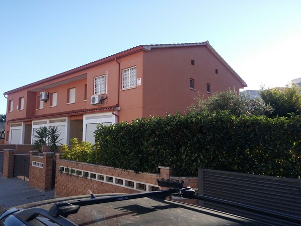 A two-story house with a red facade, white garage doors, and a brick wall with a gate.