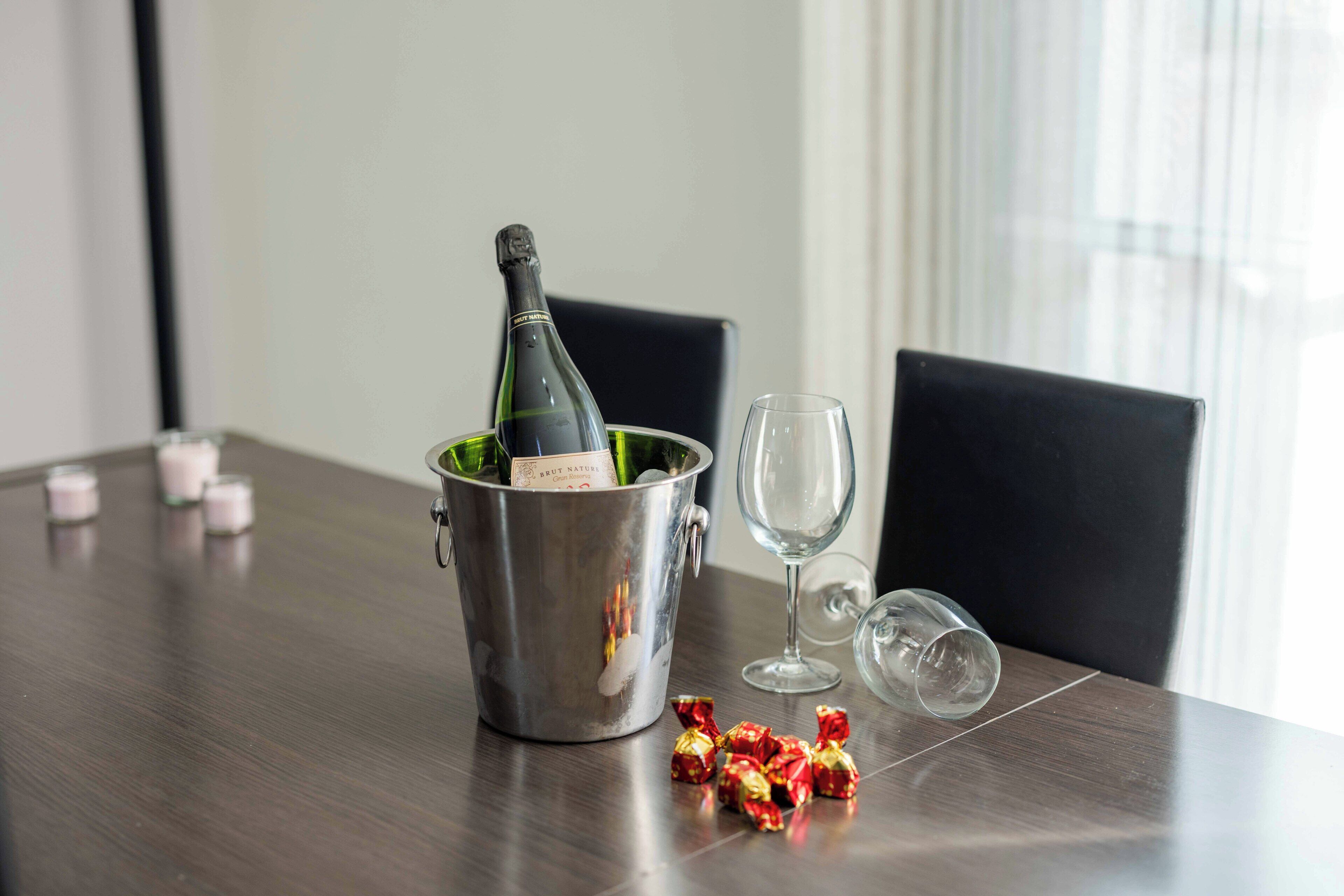 A dining table with a champagne bottle in a bucket, a wine glass, and some wrapped chocolates.