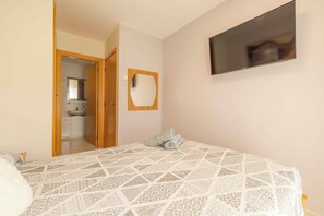 A bedroom with a patterned bedspread, a mirror, and a TV on the wall.