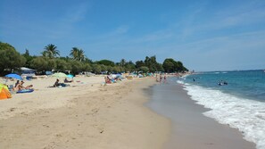 A beach with tents and umbrellas, people relaxing, and the ocean.