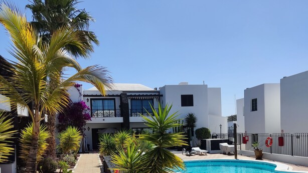 A pool area with a clear pathway, palm trees, and a building with a white facade. -  "A true haven"  spacious Apartment in a small quiet complex nearby the beach (Puerto del Carmen)
