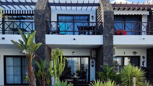 A modern two-story building with a patio area featuring various plants and a tiled walkway. -  "A true haven"  spacious Apartment in a small quiet complex nearby the beach (Puerto del Carmen)