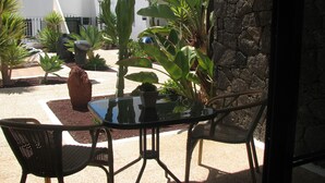 An outdoor patio with a glass table and chairs, surrounded by various plants and a stone wall. -  "A true haven"  spacious Apartment in a small quiet complex nearby the beach (Puerto del Carmen)