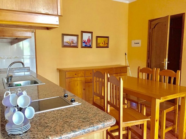 A kitchen with granite countertops, a sink, a dining table with chairs, wooden cabinets, and three framed pictures on the wall.