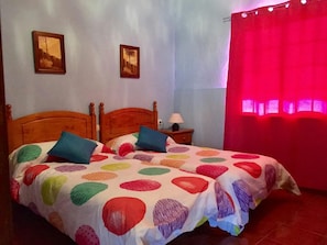 A bedroom with a double bed, two pillows, a nightstand with a lamp, and two framed pictures on the wall.