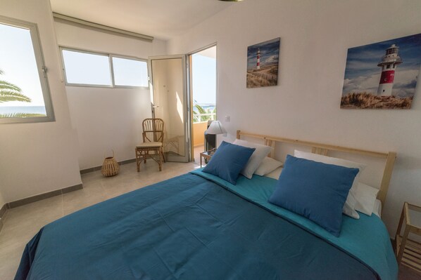 A bedroom with a large bed, a chair, a small table, and a painting of a lighthouse.