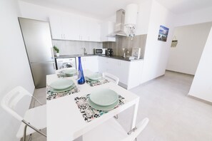A modern kitchen with white cabinets, a stainless steel refrigerator, and a dining area with a white table set for two.
