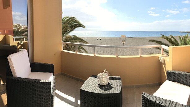 A balcony with wicker furniture, a small table with a lantern, and a view of the beach and ocean. - Ocean View apartments. Beachfront Ocean view terrace. Wifi. Parking (Gran Tarajal)