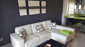 Een moderne woonkamer met een witte leren bank, een groene plaid en abstracte wanddecoratie.