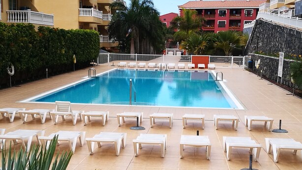 A swimming pool with white lounge chairs and a tiled deck. - Apartment in El Palm-Mar, Arona, very well decorated, furnished and equipped. (Palm-Mar)