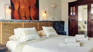 Un lit bien fait, avec du linge de lit et des serviettes blanches, une tête de lit en bois, un mur d’accent en pierre et une armoire en bois.