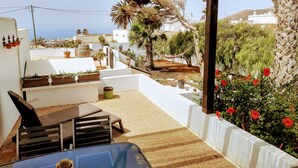 Un espace extérieur abrité, avec une table et des chaises, entouré de plantes en pot et offrant une vue sur la mer.