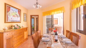 A dining area with a table set for six, wooden chairs, a cabinet, and a painting on the wall. - VILLA BELLA LUCIA 2 "heated pool, wifi, barbecue, tv satelite (Corralejo)