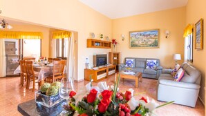 A living room with a dining area, a sofa, a TV, and a painting on the wall. - VILLA BELLA LUCIA 2 "heated pool, wifi, barbecue, tv satelite (Corralejo)