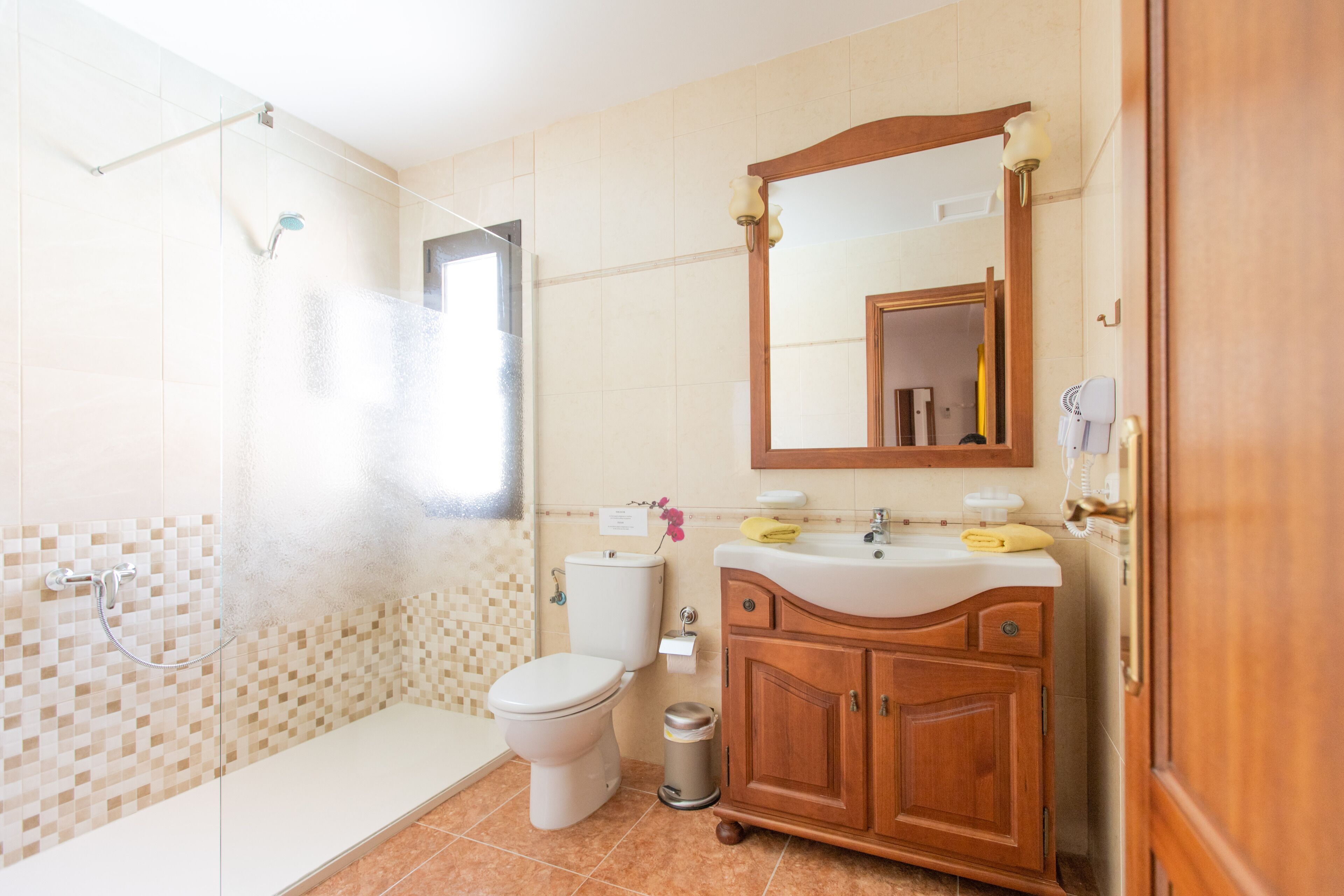 A bathroom with a shower, toilet, sink, and wooden cabinet.