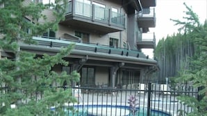 A multi-story building with balconies, a swimming pool, and surrounding greenery.