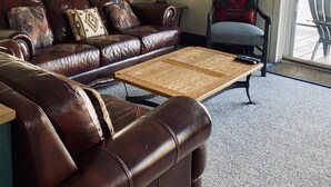 A living room with a brown leather sofa, a wooden coffee table, a lamp, a chair, and a wreath on the wall.